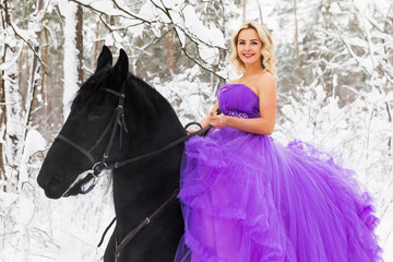 Fototapeta premium Young woman in long dress riding a horse in winter