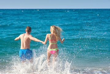 Caucasian man and woman running into the sea water. Back view.