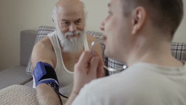 Doctor check pulse of old man with tonometer