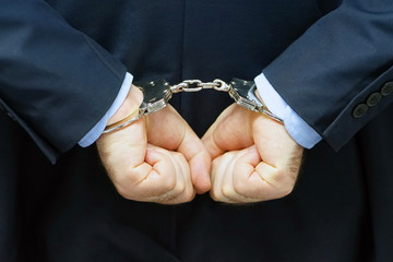 Close-up. Arrested man handcuffed hands at the back. Businessman in office in handcuffs holding a...