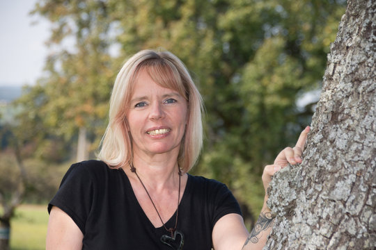 Blonde Frau steht unter Apfelbaum im Sommer
