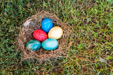 Colorful easter eggs in nest on grass, top view