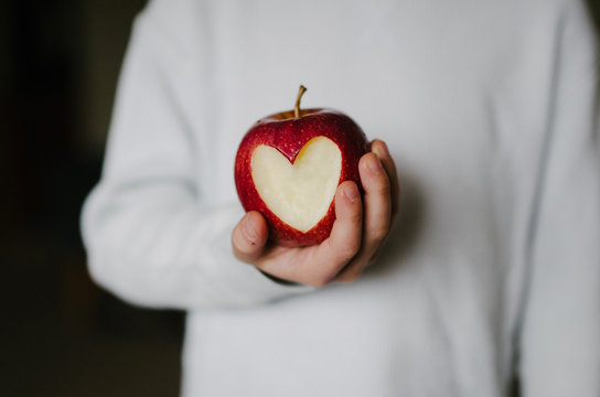 Close-up of hand holding red apple with heart shape