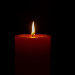 Single red orange candle lit on black background 