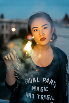 Young woman with sparkler firework in hand on rooftop at dusk