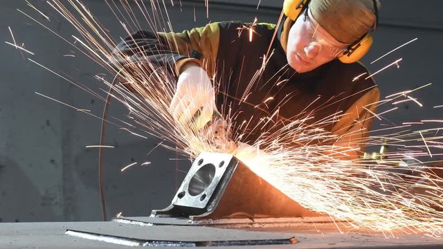 worker grinding weld seam with grinder machine and sparks