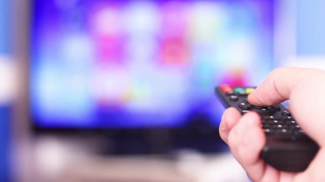 Close-up hand on television remote and tv screen.
