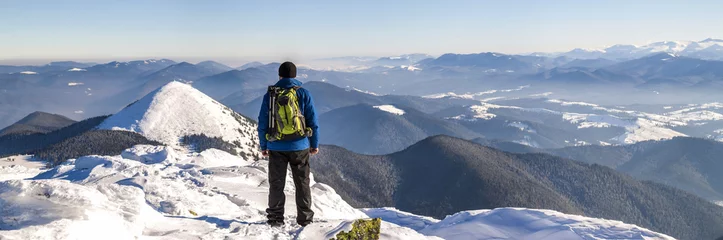 Gordijnen Man hiker on top of a mountain in winter © bilanol