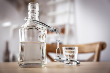 Bottle and glass of alcohol with handcuffs on wooden table. Concept of alcohol dependence