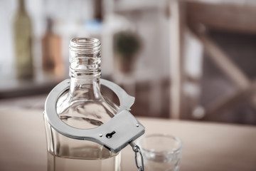 Bottle of alcohol with handcuffs on table. Concept of alcohol dependence
