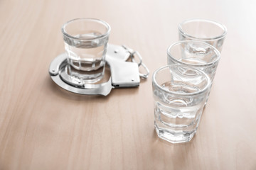 Glasses of alcohol with handcuffs on wooden table. Concept of alcohol dependence