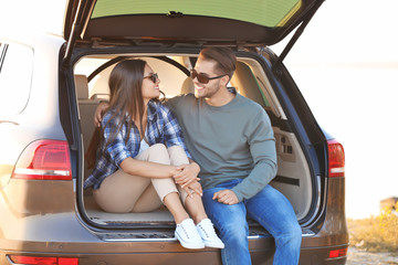 Beautiful young couple sitting in car  trunk
