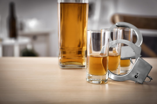 Glassware of alcohol with handcuffs on wooden table. Concept of alcohol dependence