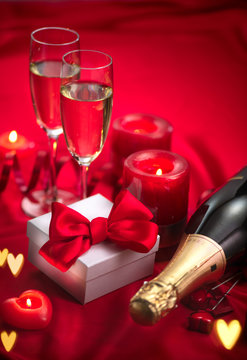 Valentine's Day romantic dinner. Date. Champagne, candles and gift box over holiday red background