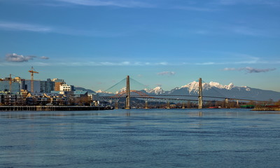 Residential District in New Westminster City with new construction at the waterfront of   Fraser River and three bridges at the bakground of blue ske and snow caped mountain range 