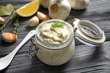 Tasty sauce with garlic in jar on wooden table