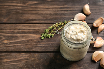 Tasty sauce with garlic in jar on wooden table