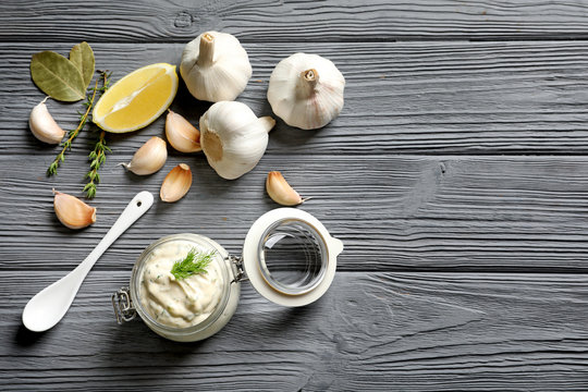Tasty sauce with garlic in jar and ingredients on wooden table