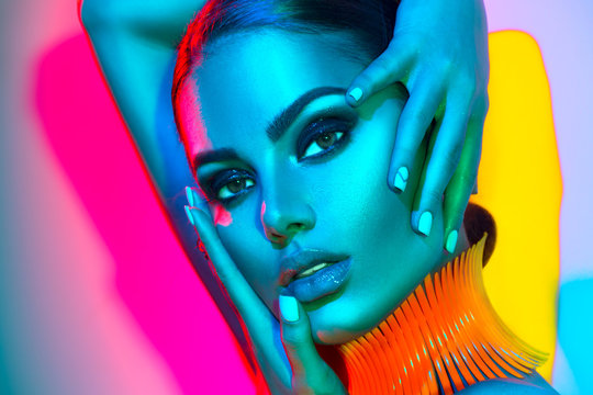 Fototapeta Fashion model woman in colorful bright lights with trendy makeup and manicure posing in studio