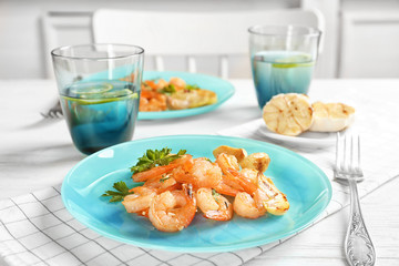 Plate with delicious fried shrimps and garlic on table