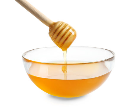 Honey pouring from wooden honey dipper into glass bowl on white background