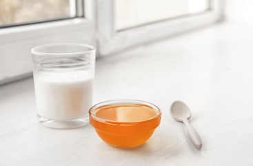 Fototapeta na wymiar Glass of milk and bowl with honey on windowsill