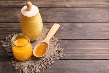 Glass jars and spoon with honey on wooden background