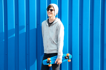 Hipster teenager with skateboard near color wall outdoors