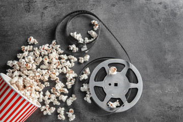 Paper cup with tasty popcorn and movie reel on grey background