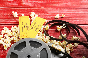 Tasty popcorn, tickets and movie reel on red wooden background