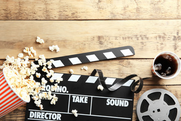 Tasty popcorn, clapboard and movie reel on wooden background