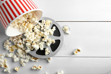 Tasty popcorn and movie reel on white wooden background
