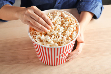 Woman eating tasty popcorn at table, closeup