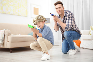 Cute boy and his father playing with toy guns at home