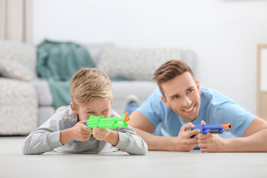 Cute boy and his father playing with toy guns at home