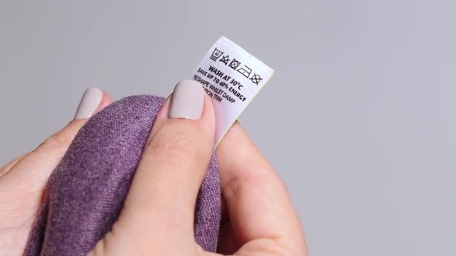 Closeup macro view of female hands of caucasian adult housewife holding clothes in hands and learning information about washing before doing laundry.