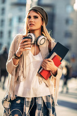 Positive cute female student dressed in stylish clothing drinking coffee to go while going to campus. 