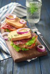Wooden board with delicious sandwiches on table