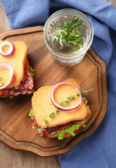 Wooden board with delicious sandwiches on table