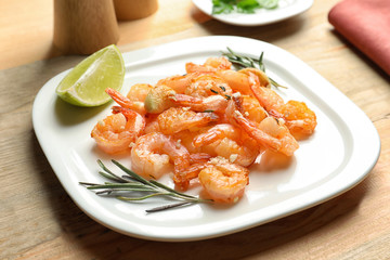 Plate with delicious fried shrimps and garlic on table