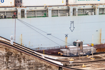 Naklejka premium GATUN, PANAMA - 29 maja 2016: Lokomotywa elektryczna, znana jako muł, prowadząca kontenerowiec przez śluzy Gatun, część Kanału Panamskiego.