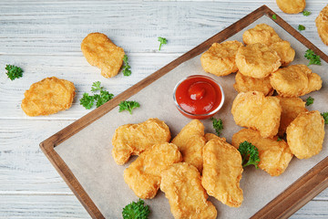 Wooden board with tasty chicken nuggets and sauce on table