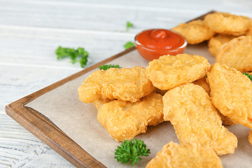 Wooden board with tasty chicken nuggets and sauce on table