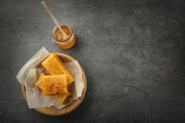 Bowl with sweet honeycombs and jar with honey on grey background