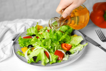Woman adding tasty apple vinegar into salad with vegetables on plate