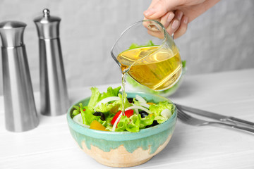 Woman adding tasty apple vinegar into salad with vegetables on table