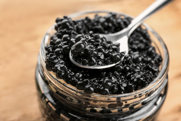 Glass jar and spoon with black caviar, closeup