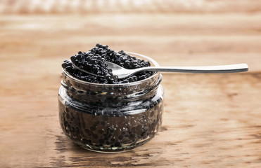 Fototapeta na wymiar Glass jar and spoon with black caviar on wooden table
