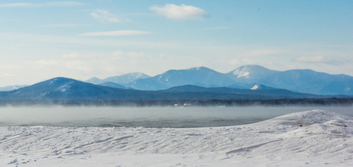 frigid winter morning with misty steam rising off the lake with the Adirondack mountains across the lake in New York 
