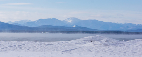 frigid winter morning with misty steam rising off the lake with the Adirondack mountains across the lake in New York 
